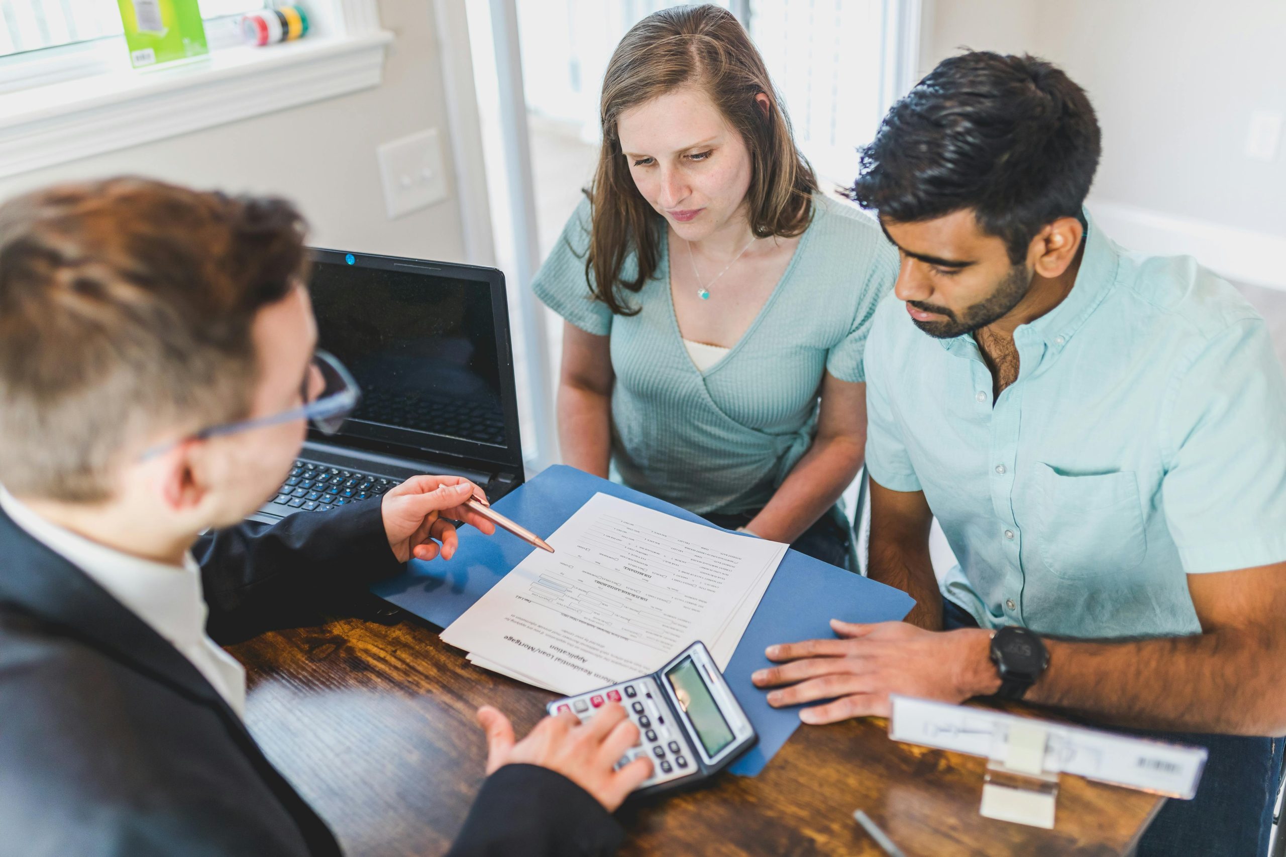couple and man in a suit sitting at a desk with a laptop, a calculator, and documents