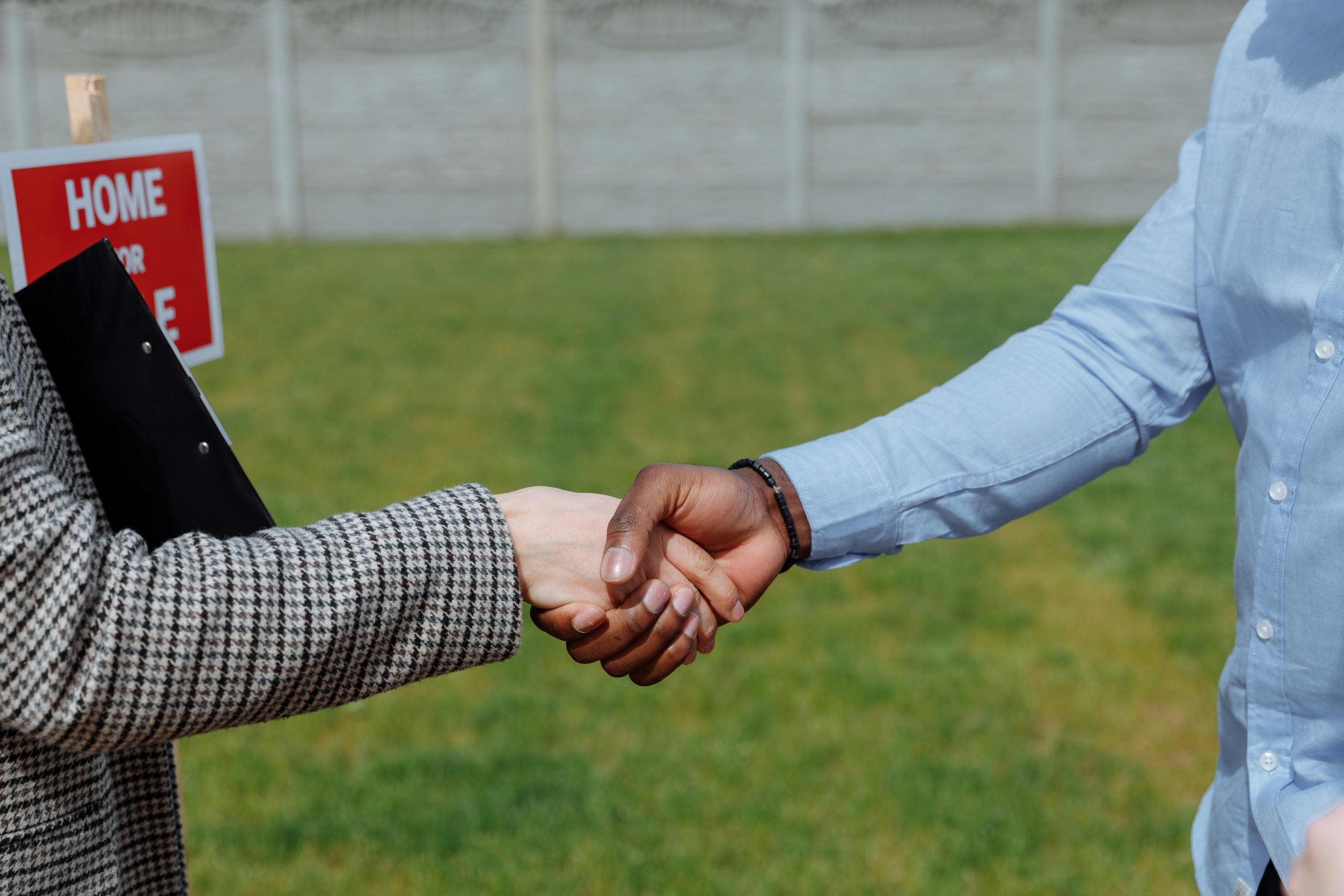 home buyer and seller shaking hands next to a 'home for sale' sign