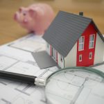 a miniature house, a magnifying glass, and a piggy bank on a wooden surface